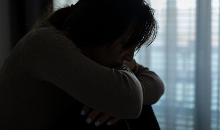 Imagen en sombre de la silueta de una mujer sentada, aparentemente entristecida.