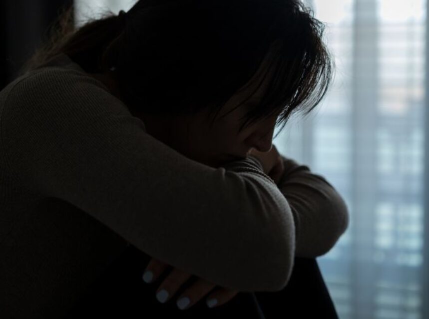 Imagen en sombre de la silueta de una mujer sentada, aparentemente entristecida.