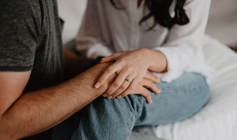 Una pareja sentados sobre una cama o sofá, tocan sus manos uno a otro.