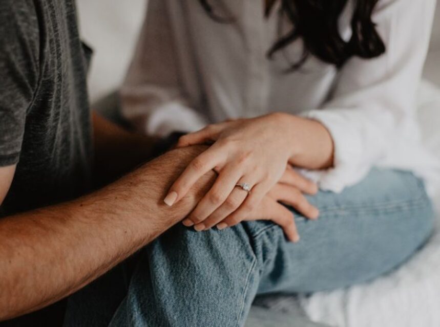 Una pareja sentados sobre una cama o sofá, tocan sus manos uno a otro.