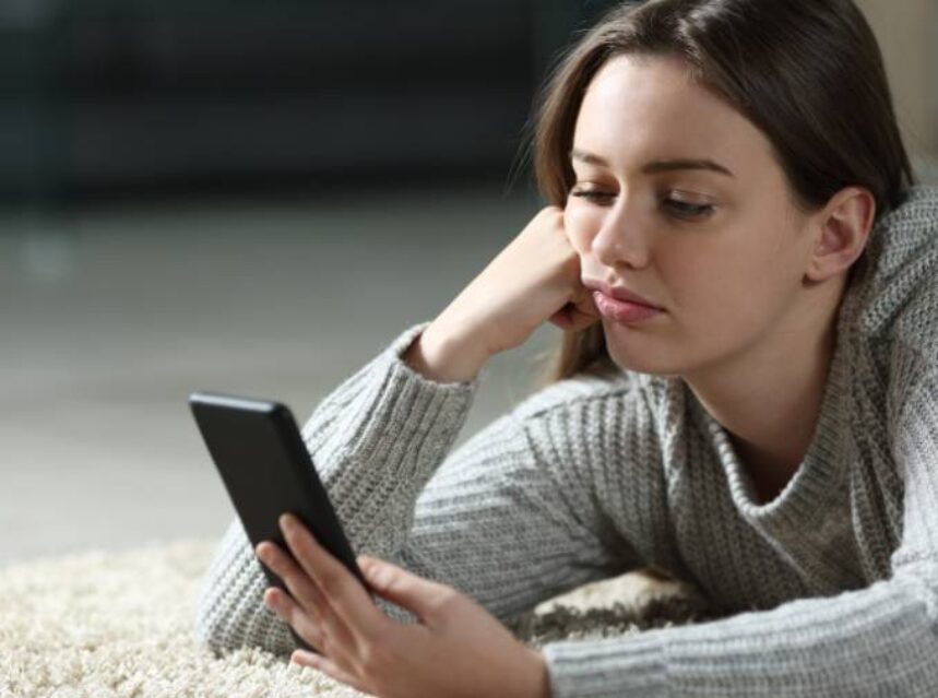 a woman lying on the floor bored looking at a phone