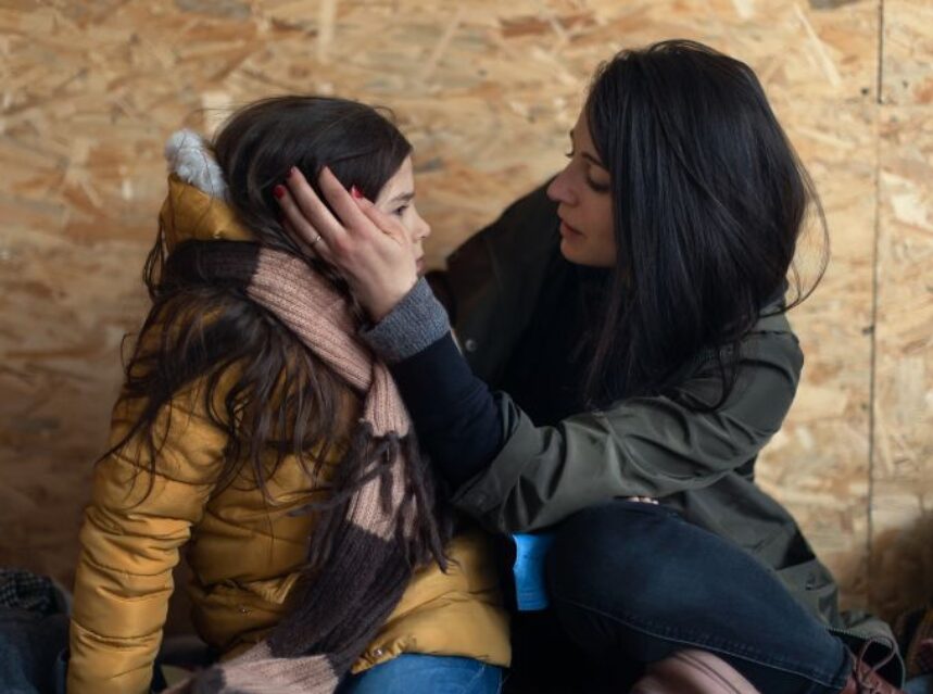 Una madre con su hija, le acaricia el rostro. Están sentadas en el piso en un refugio temporal.