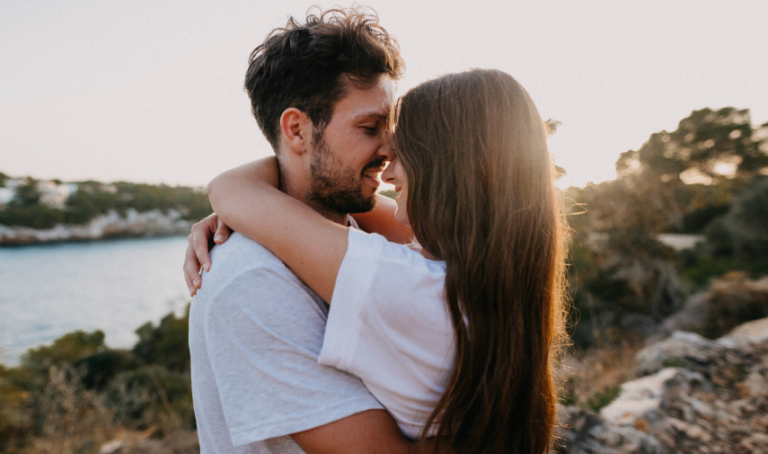 Una pareja se abraza tiernamente con un paisaje natural al fondo.