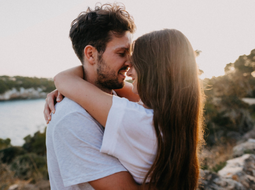 Una pareja se abraza tiernamente con un paisaje natural al fondo.