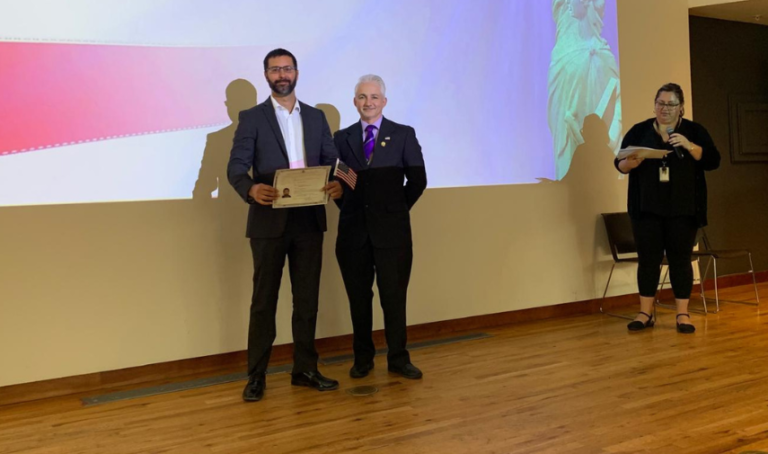 two men standing in front of a projector screen. Aprende como ser ciudadno americano