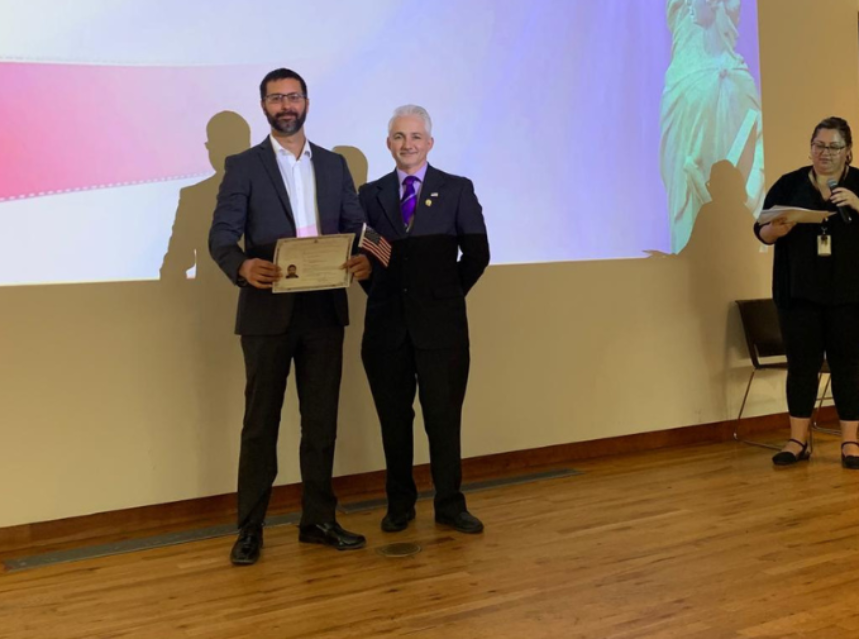 two men standing in front of a projector screen. Aprende como ser ciudadno americano