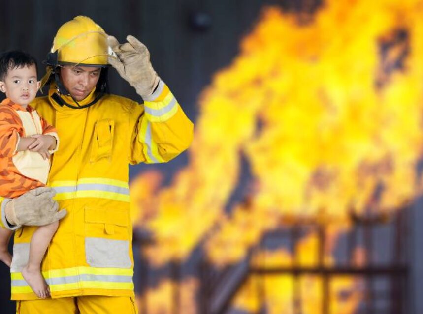 a firefighter holding a kid putting on a helmet