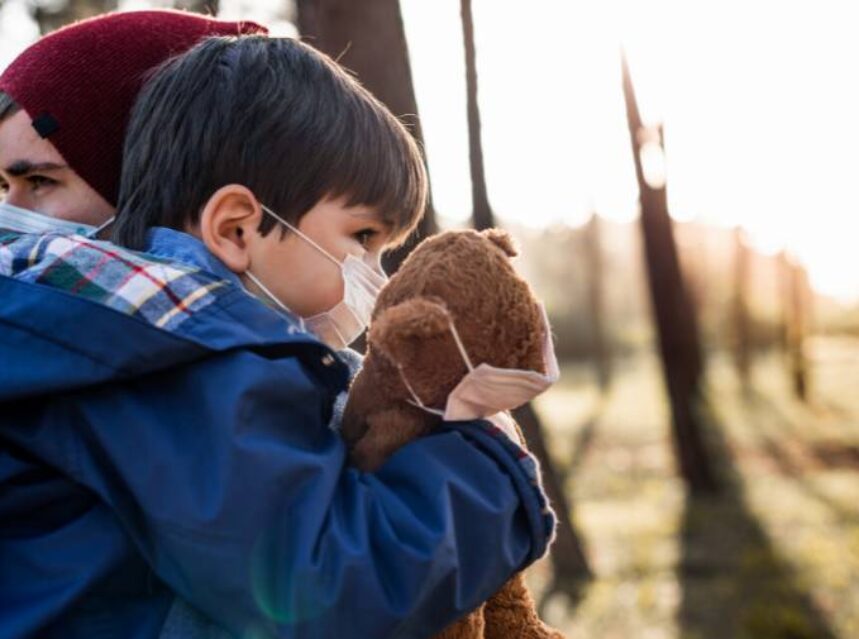 a child holding a teddy bear wearing a face mask